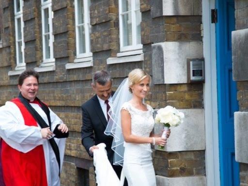 A bride and groom entering the church with a priest nearby.
